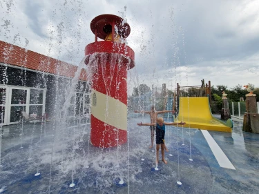 Kind speelt bij spuitende fonteinen naast vuurtoren in waterspeeltuin van De Zeeuwse Kust