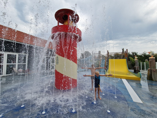 Kind speelt bij spuitende fonteinen naast vuurtoren in waterspeeltuin van De Zeeuwse Kust