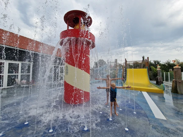 Kind speelt bij spuitende fonteinen naast vuurtoren in waterspeeltuin van De Zeeuwse Kust