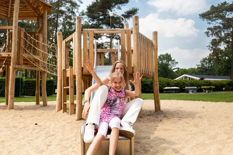 Meisje zit op een houten speeltoestel in de buitenlucht op Recreatiepark 't Gelloo.