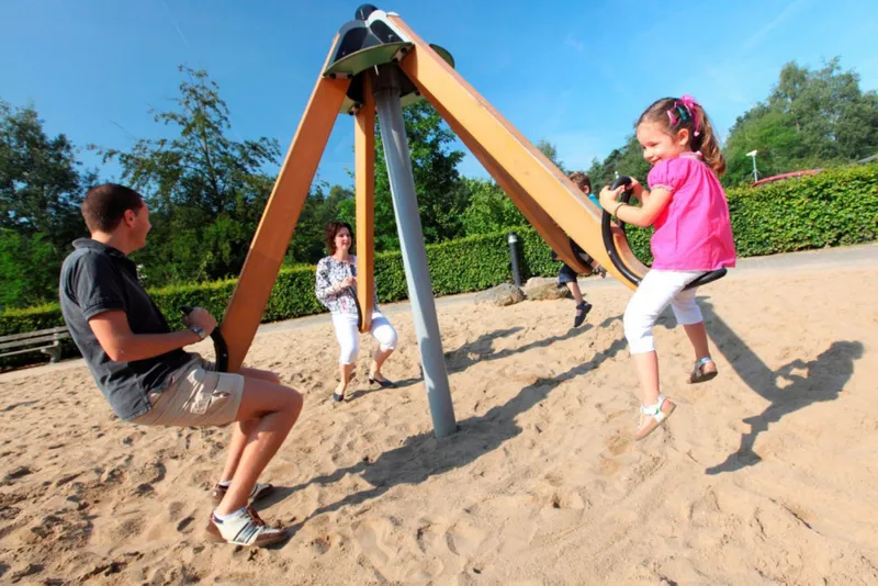 Een vader en dochter spelen samen op een houten wipwap in de zandspeeltuin van Bospark De Schaapskooi.
