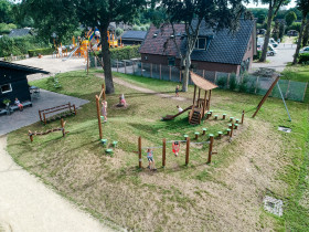 Overzicht van een natuurspeeltuin met een uitdagend balansparcours gemaakt van houten paaltjes en balken op Recreatiepark de Boshoek.