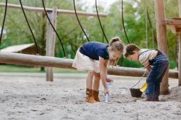 Twee kinderen spelen samen met schepjes en emmers in de grote zandbak van een natuurspeeltuin op de Beekse Bergen.