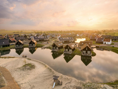Luchtfoto van Dormio Resort Nieuwvliet-Bad bij zonsondergang, met een overzicht van de vele waterwoningen rondom het water en een zandstrandje.