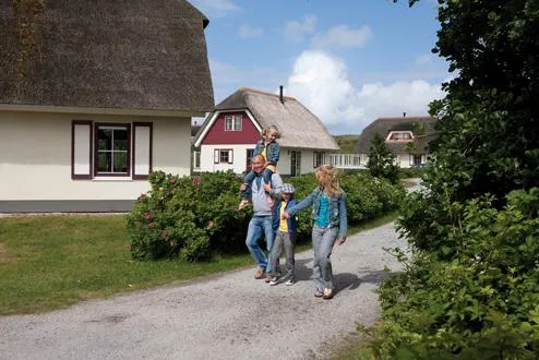 Een vrolijk gezin wandelt over een pad langs de vakantiehuisjes op het ruim opgezette Vakantiepark Boomhiemke op Ameland.