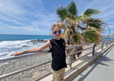 Kind staat op boulevard aan het strand met plambomen