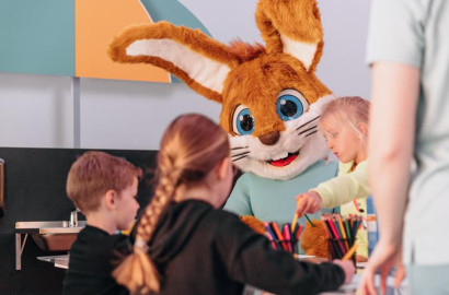 Mascotte Koos Konijn knutselt gezellig samen met een groepje kinderen aan een tafel in de Koos Kids Club.