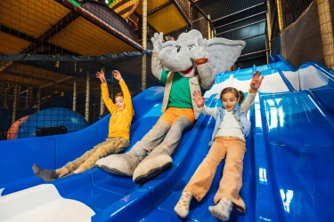 Twee kinderen glijden lachend van een blauwe glijbaan met mascotte Djambo in Speelland Beekse Bergen