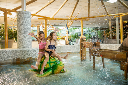 Twee meisjes spelen lachend op een groene speelgoedschildpad in het Kinder-doe-bad van de Aqua Mundo bij Center Parcs Zandvoort.