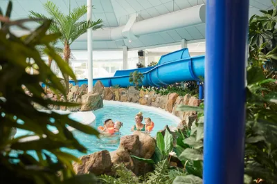 Kinderen dobberen in zwembanden in de lazy river van het subtropisch zwembad op Recreatiepark De Leistert, omgeven door rotsen en palmbomen.