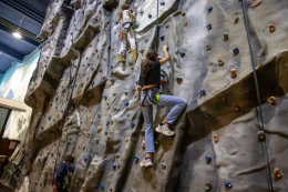 Kinderen en volwassenen die de hoge indoor klimwand bij Lalandia Billund beklimmen, gezekerd met touwen.