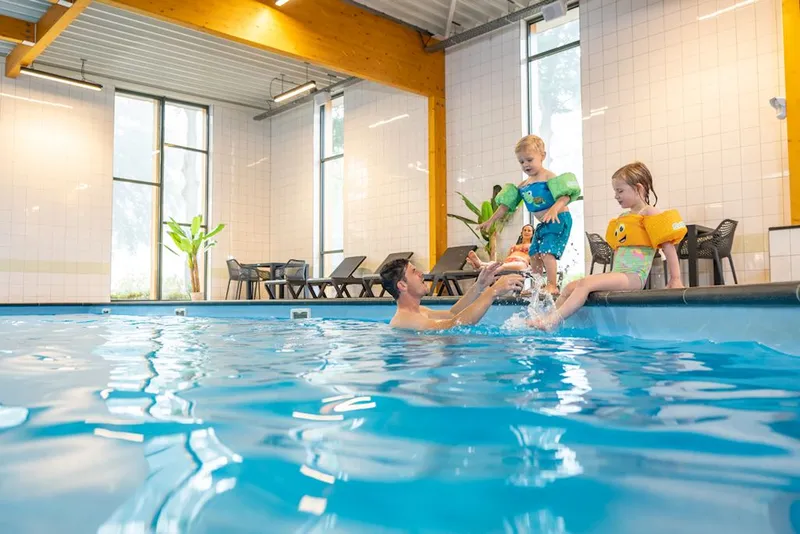 Vader met twee kinderen aan het spelen en spetteren in het overdekte binnenzwembad op vakantiepark Landal De Vlinderhoeve in Gelderland.