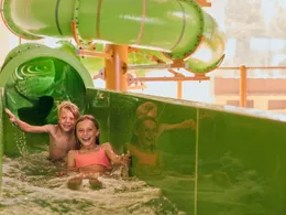 Twee kinderen komen lachend uit een groene waterglijbaan en maken een grote plons in het zwembad van de Beekse Bergen.
