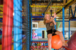 Een meisje heeft plezier in de binnenspeeltuin van Kampeerdorp De Zandstuve. Ze zit op een oranje bal aan een kabelbaan