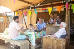 Een gezelschap geniet van een drankje en een hapje op het gezellige, overdekte terras bij de horeca van Camping 't Veld.