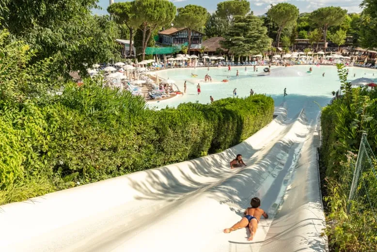 Kinderen glijden van de brede, heuvelachtige waterglijbaan zo het lagune zwembad in op Camping Altomincio Family Park.