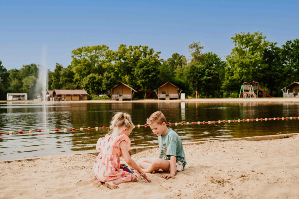 Twee kinderen spelen in het zand op het strand bij de zwemvijver van Vakantiepark Dierenbos