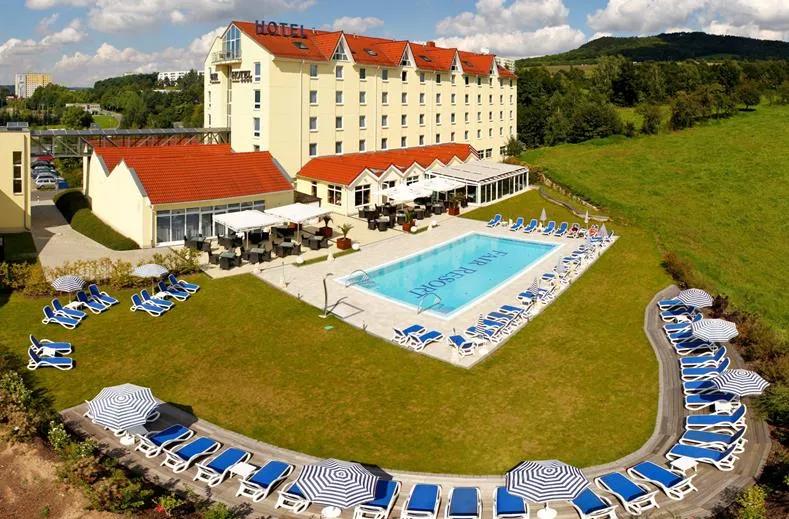 Panoramisch overzicht van het FAIR Resort in Thüringen, met het hotel, het grote buitenzwembad en de omringende groene ligweide voor gezinnen.