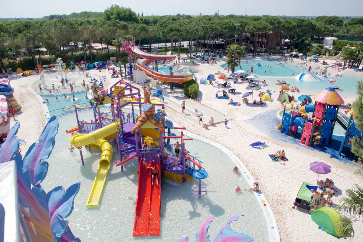 Overzicht van de kleurrijke waterspeeltuin in een van de aquaparken op Camping Union Lido, vol met glijbanen, speeltoestellen en spetterende kinderen.