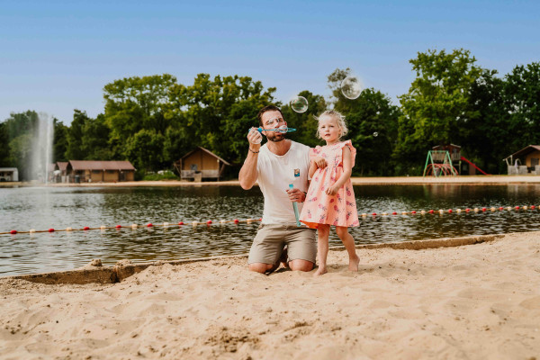 Vader en dochter spelen op zandstrand bij zwemvijver Vakantiepark Dierenbos