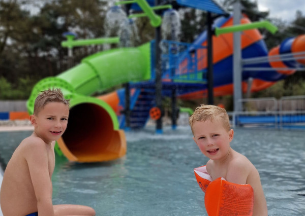 Kinderen zitten in het kinderzwembad bij De Zandstuve en kijken uit over de waterspeeltuin met glijbanen