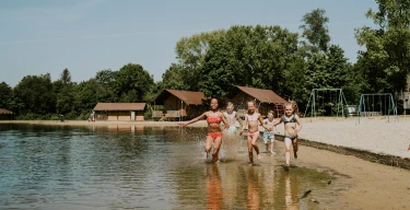 Kinderen rennen en spelen in het water bij het strand van de zwemvijver van Vakantiepark Dierenbos
