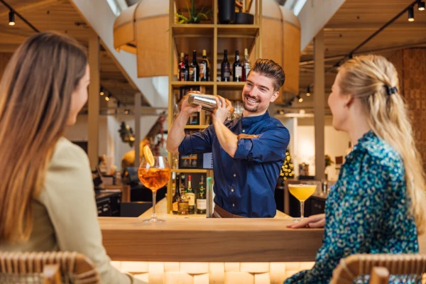 Een lachende bartender schudt een cocktail voor twee gasten aan de bar van Safari Hotel Beekse Bergen