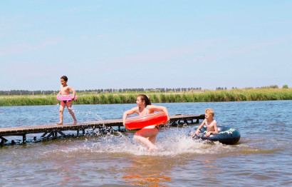 Kinderen springen en spelen met zwembanden vanaf een houten steiger in de recreatieplas van Vakantiepark Marina Beach.