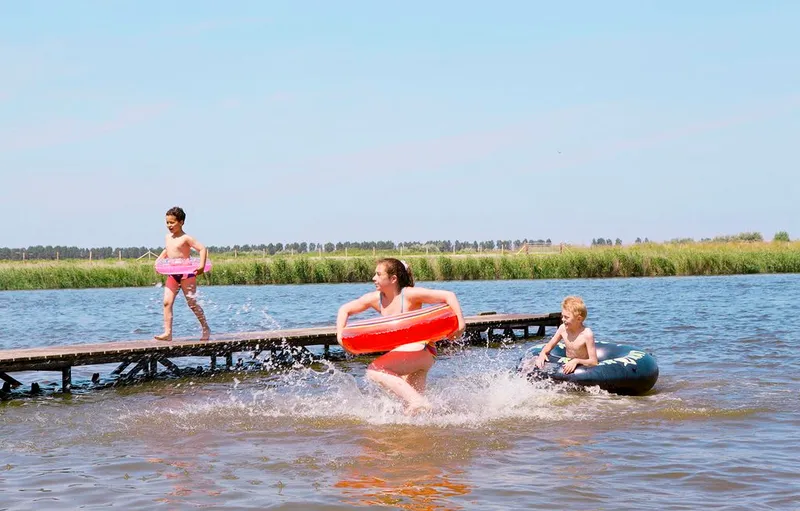 Kinderen springen en spelen met zwembanden vanaf een houten steiger in de recreatieplas van Vakantiepark Marina Beach.