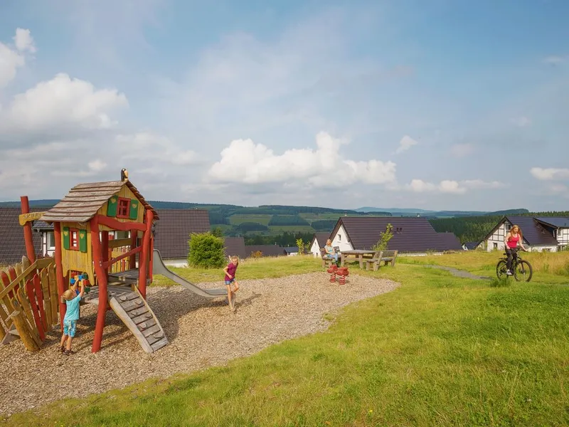Kinderen spelen op de houten klimtoestellen in de buitenspeeltuin van Landal Winterberg, met uitzicht over het heuvelachtige landschap.