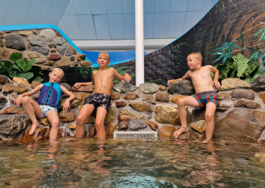 Kinderen zitten op rand van een rotswand in subtropisch zwembad van vakantiepark de leistert