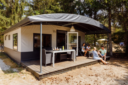 Een gezin geniet op de overdekte veranda van een moderne chalet, gelegen in de bosrijke omgeving van RCN het Grote Bos in Utrecht.