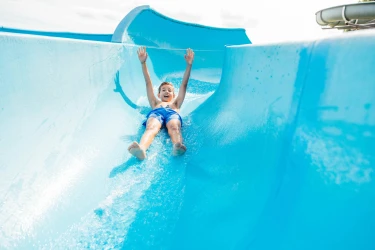 Lachende jongen glijdt met opgestoken armen van grote blauwe waterglijbaan in zwembad van Safari Hotel Beekse Bergen