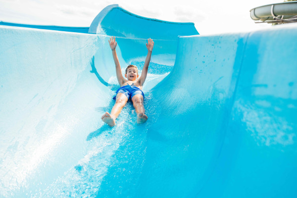 Lachende jongen glijdt met opgestoken armen van grote blauwe waterglijbaan in zwembad van Safari Hotel Beekse Bergen