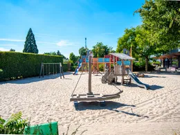 Een speeltuin met een houten speelschip, glijbaan en schommels in een grote zandbak op Landal Marina Resort Well.