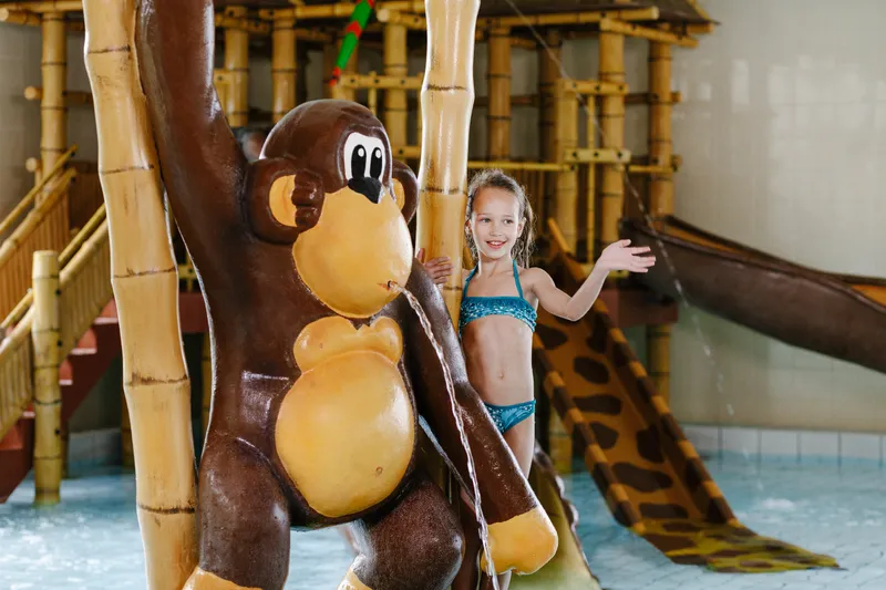 Een meisje poseert naast een groot apenbeeld in het jungle-binnenzwembad van Camping Beekse Bergen.