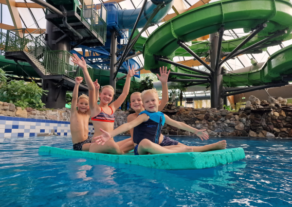 Kinderen in suptropisch zwembad op een mat met kleurrijke glijbanen op de achtergrond
