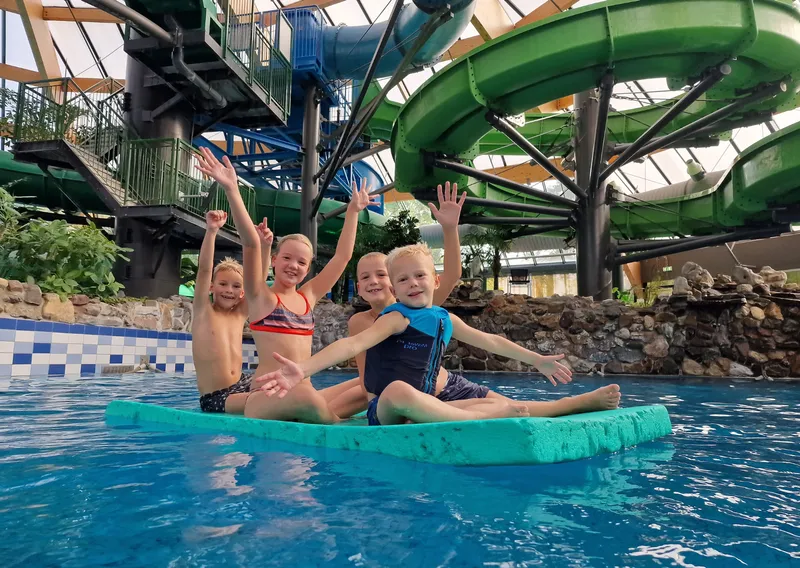 Kinderen in suptropisch zwembad op een mat met kleurrijke glijbanen op de achtergrond