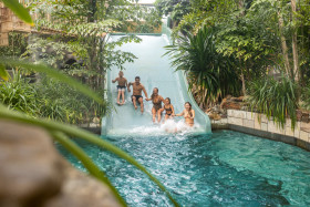 Een groep van vijf vrienden glijdt tegelijkertijd lachend naar beneden van de extra brede familieglijbaan in het tropische zwemparadijs Aqua Mundo van De Eemhof.