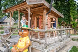 Kinderen spelen bij het houten speelhuisje van Bollo, met een standbeeld van de mascotte ervoor.