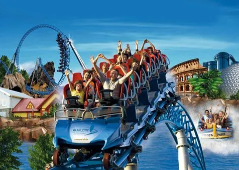 Bezoekers in de spectaculaire achtbaan Blue Fire Megacoaster in Europa-Park, met een looping en andere attracties op de achtergrond.