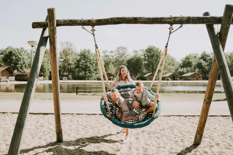 Schommel_activiteit_kinderen_Zwemmen_Kindvriendelijk_vakantiepark_DierenbosMoeder en twee kinderen op grote nestschommel bij strand en zwemvijver van Vakantiepark Dierenbos