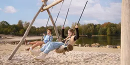 Twee kinderen hebben plezier op een grote touwschommel op het strand, met uitzicht op het Victoriameer