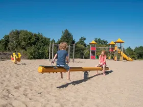 Kinderen spelen samen op een wip en andere speeltoestellen in de grote zandspeeltuin van Landal Beach Resort Ooghdyne.
