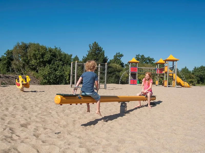 Kinderen spelen samen op een wip en andere speeltoestellen in de grote zandspeeltuin van Landal Beach Resort Ooghdyne.
