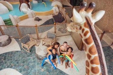Gezin speelt met zwemschuimen in het binnenzwembad met safarithema en grote giraffebeeld bij Safari Resort Beekse Bergen