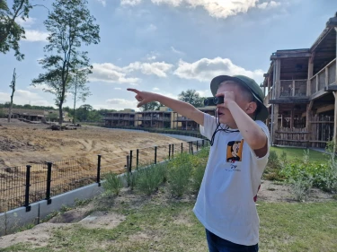 Kind kijkt door verrekijker en wijst naar dieren bij Beekse Bergen