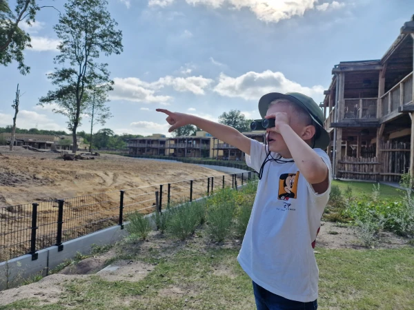 Kind kijkt door verrekijker en wijst naar dieren bij Beekse Bergen