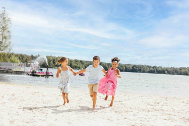 Drie lachende kinderen rennen hand in hand over het zandstrand van Lake Resort Beekse Bergen