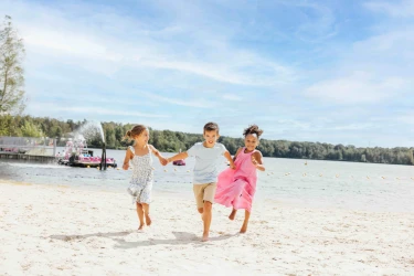 Drie lachende kinderen rennen hand in hand over het zandstrand van Lake Resort Beekse Bergen